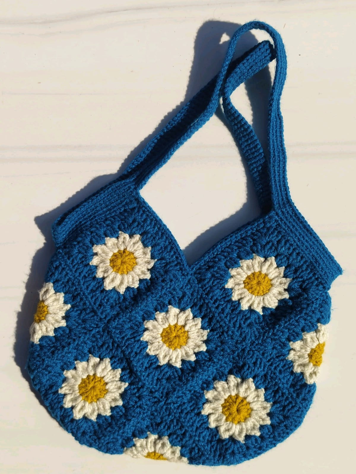 Blue crochet bag with white daisy flowers on a light wooden surface