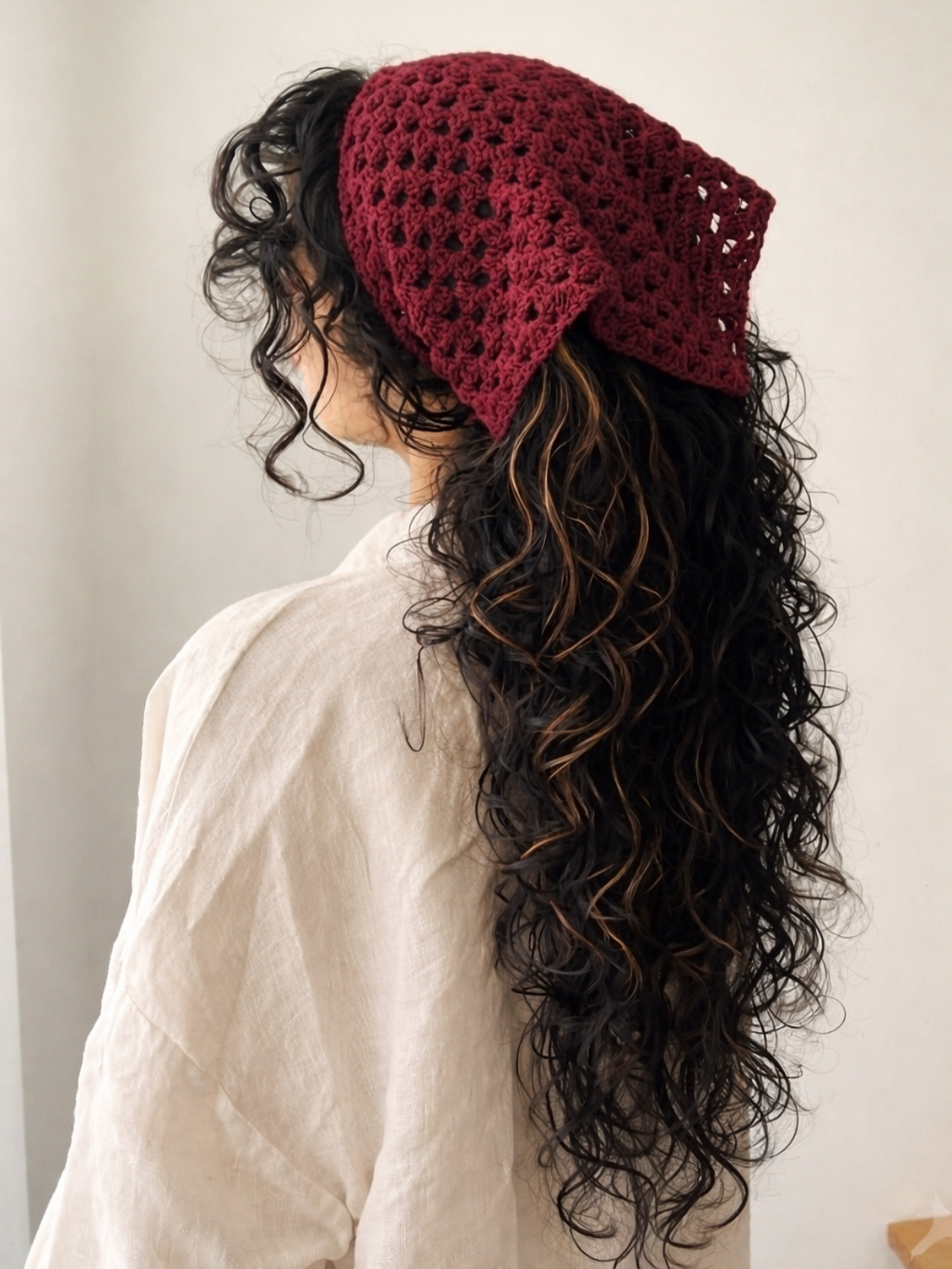 Person wearing a red knitted headband with long, wavy hair on a plain background