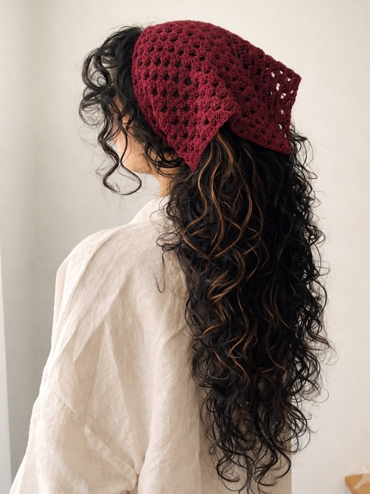 Person wearing a red knitted headband with long, wavy hair on a plain background