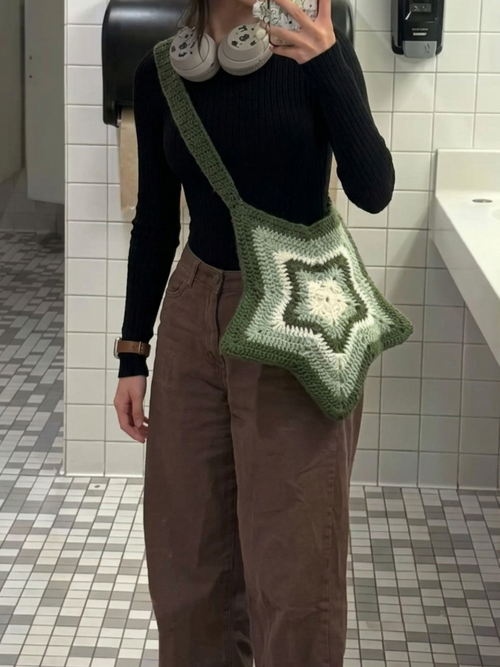 Person taking a mirror selfie in a bathroom wearing a green star-patterned bag.