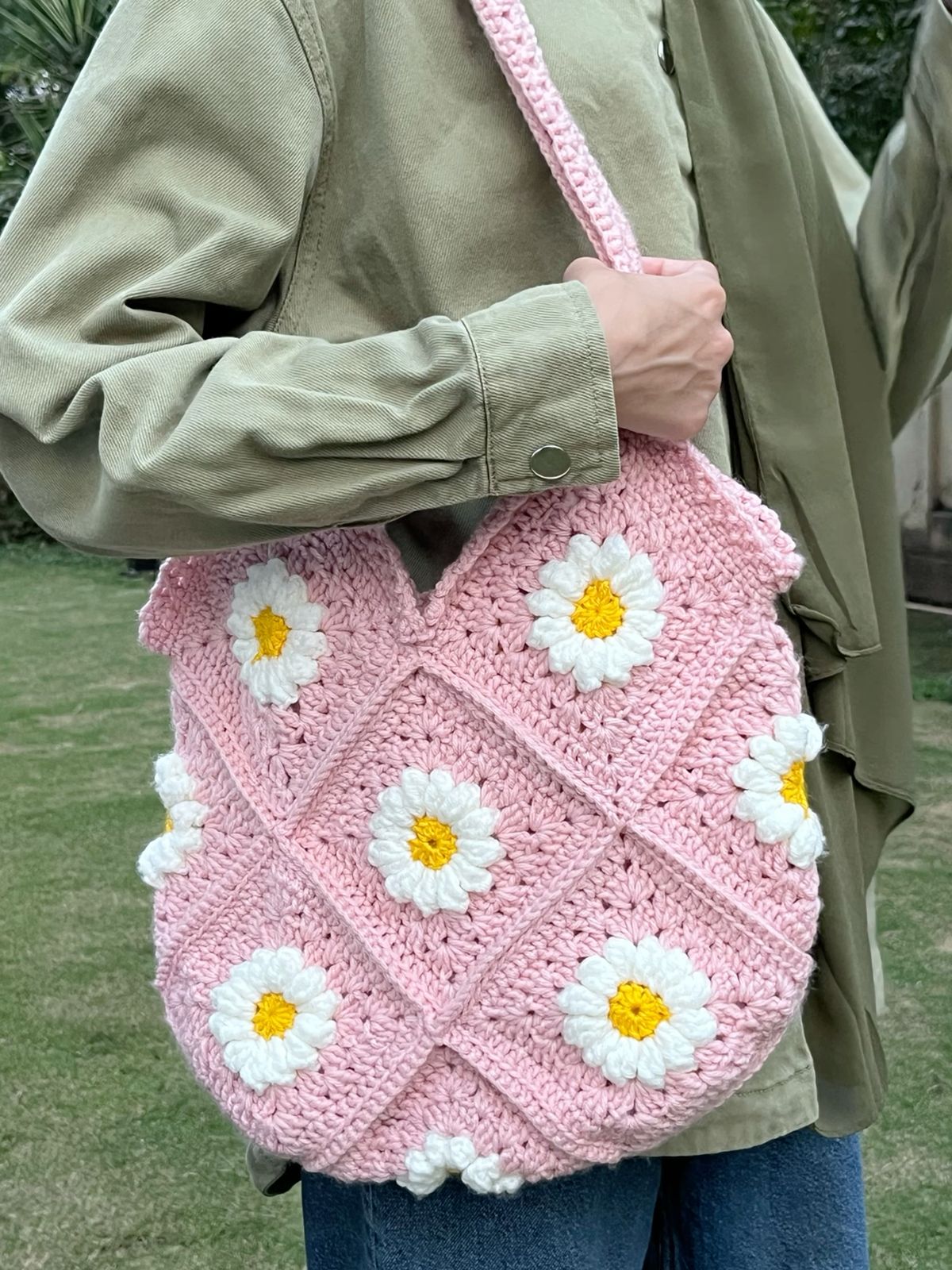 Pink crochet bag with daisy patterns held by a person outdoors.