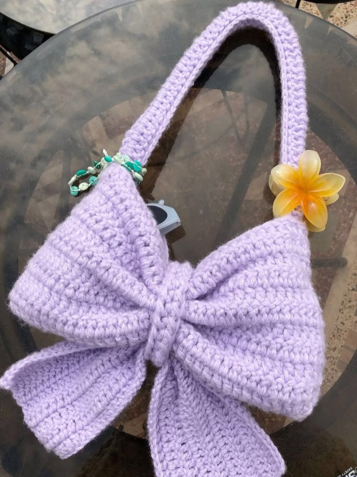 Purple crocheted bag with a yellow flower on a reflective surface