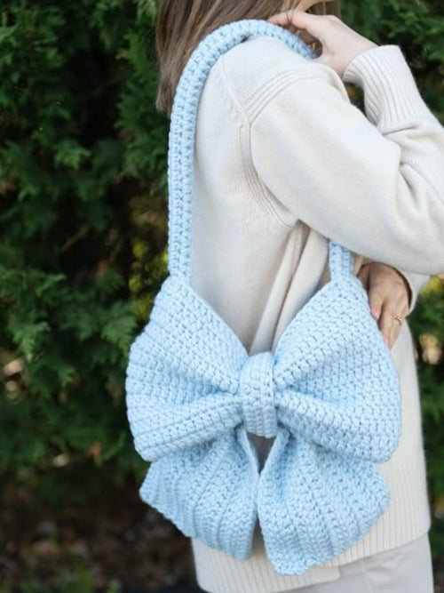Light blue knitted bow held by a person against a blurred green background