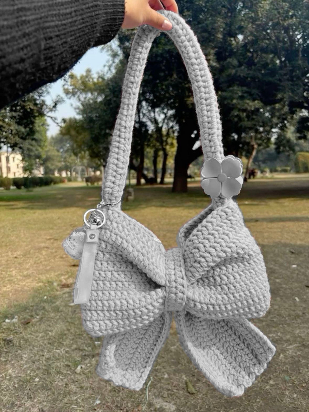 Brown crochet bow bag held by a hand with a park background