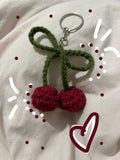 Crocheted cherry keychain on a white background with decorative elements.