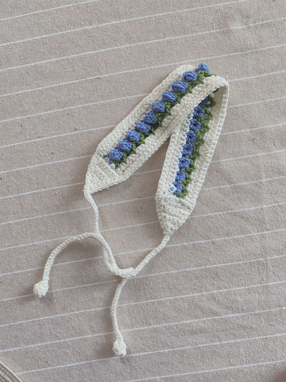 Crocheted headband with blue and green floral patterns on a textured surface