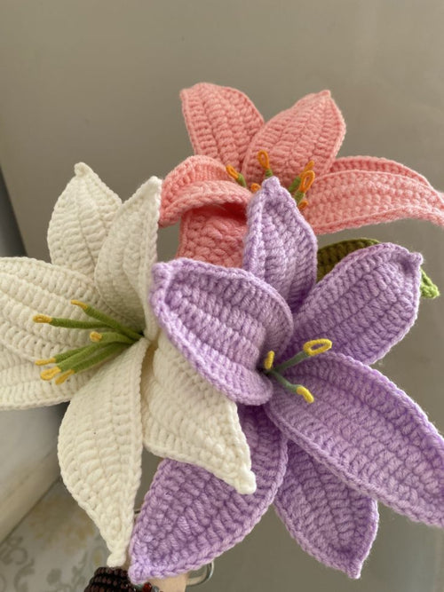 Three crocheted flowers in pink, purple, and white on a neutral background