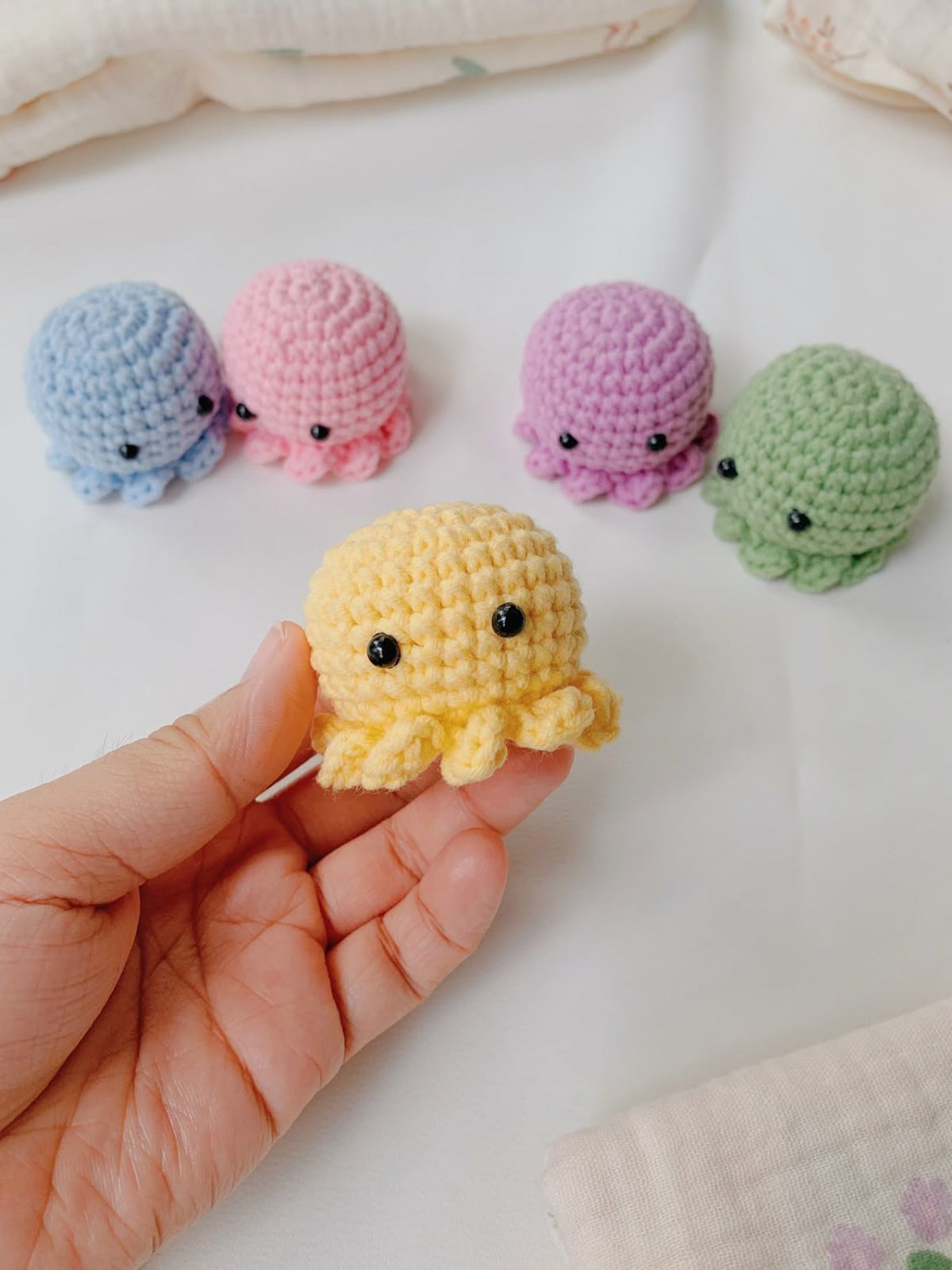 Hand holding a yellow crochet octopus toy with other colorful octopus toys on a light background.