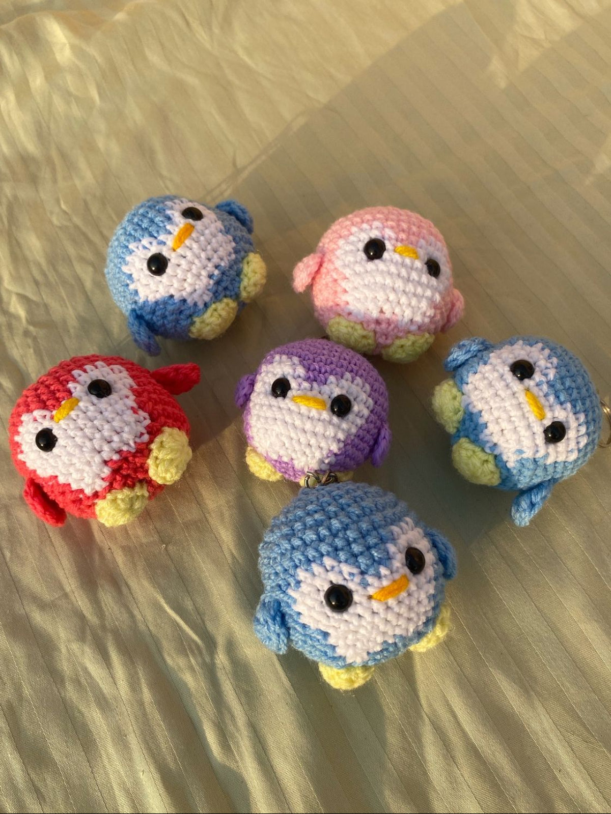Set of colorful crochet penguin keychains on a textured surface