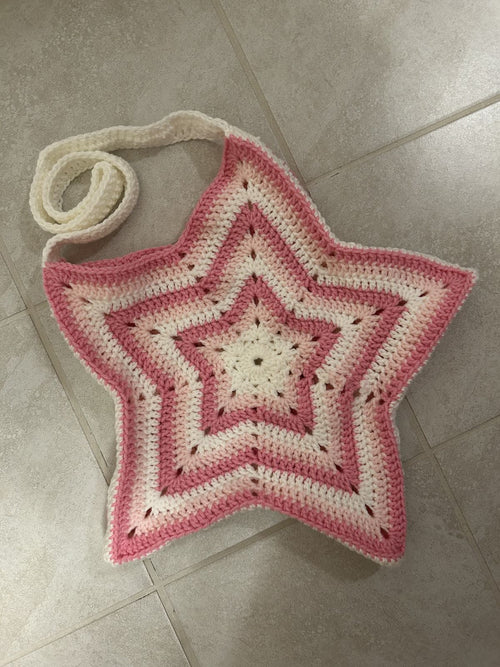 Star-shaped crochet bag with pink and white colors on a tiled floor.